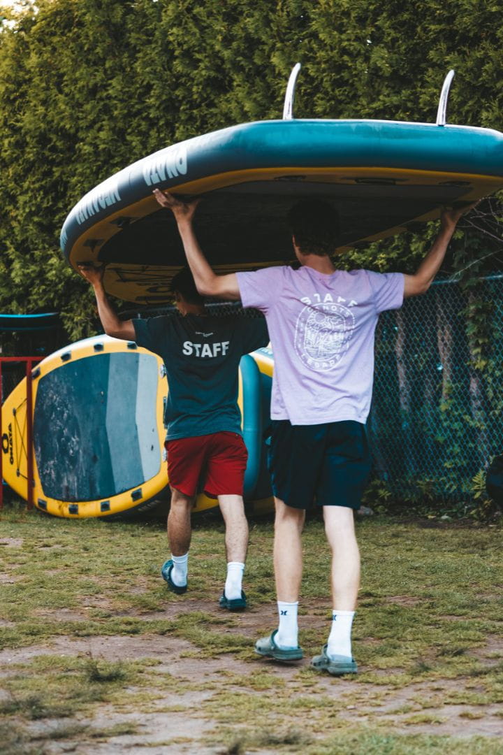 Employés Canots Légaré transportant une planche à pagaie familiale sur leurs épaules